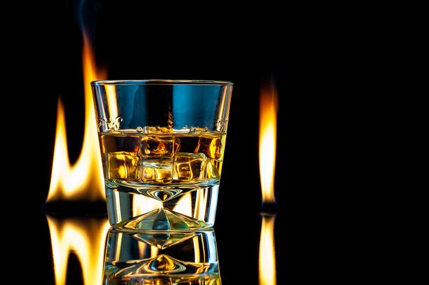 Whisky of bourbon in een transparant glas met ijsblokjes op een zwarte met vuur