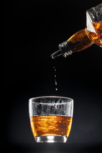 Whisky pouring into a glass on black background