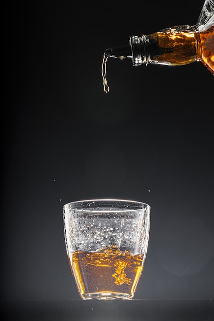 黒の背景にグラスに注ぐウイスキー