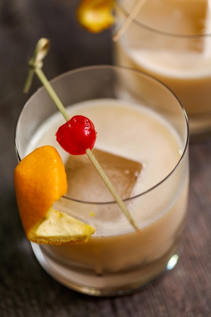 Whisky zure cocktail gegarneerd met sinaasappel en kersen.