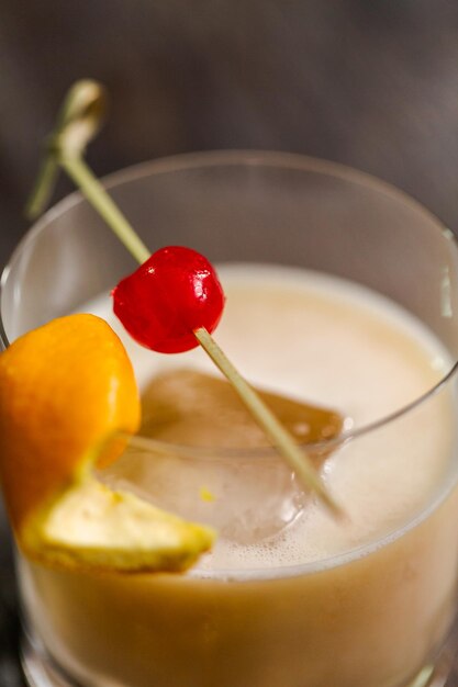 Whisky zure cocktail gegarneerd met sinaasappel en kersen.