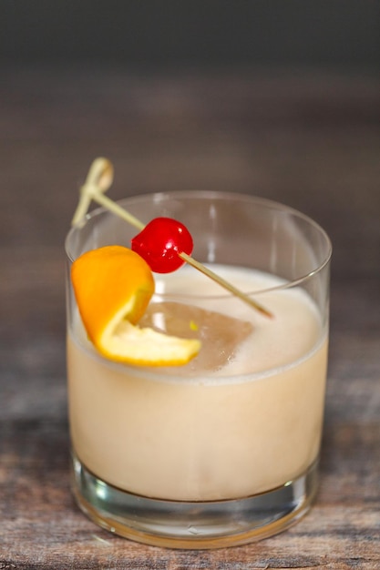 Whisky zure cocktail gegarneerd met sinaasappel en kersen.