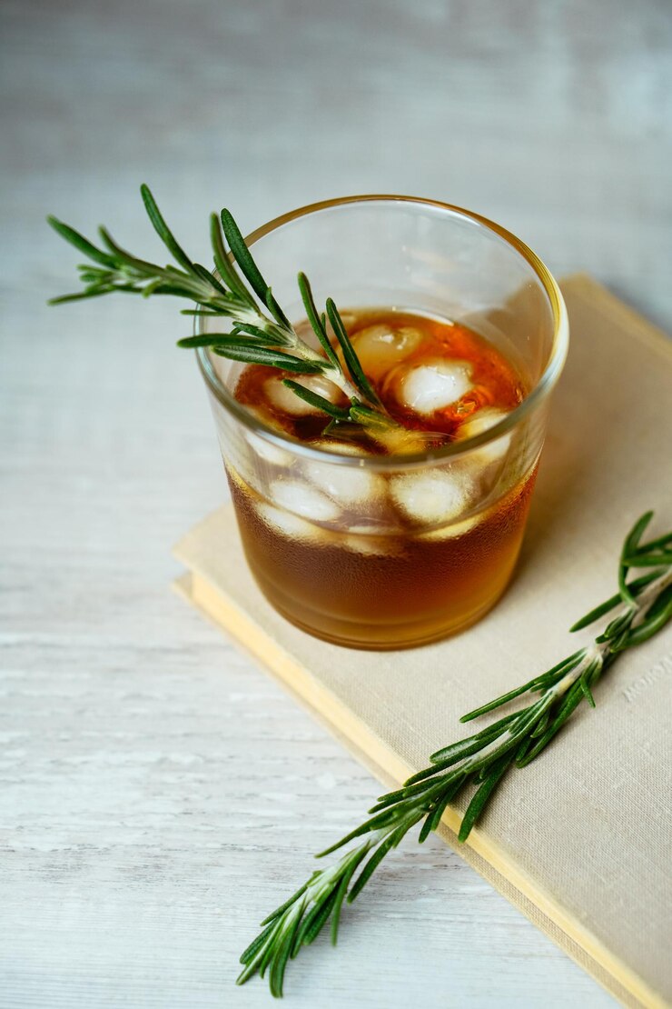 Whiskyzure cocktail met rumijs en rozemarijn in borrelglas op boek Alcoholcocktail op tafel