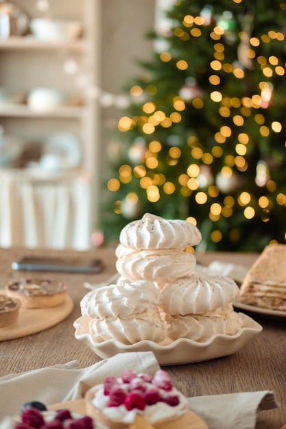 White airy meringue cake on a festive table against the background of a Christmas tree with a garland