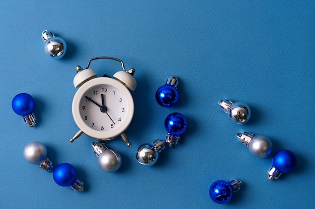 White alarm clock on a blue table with Christmas balls. The concept of the festive decorations