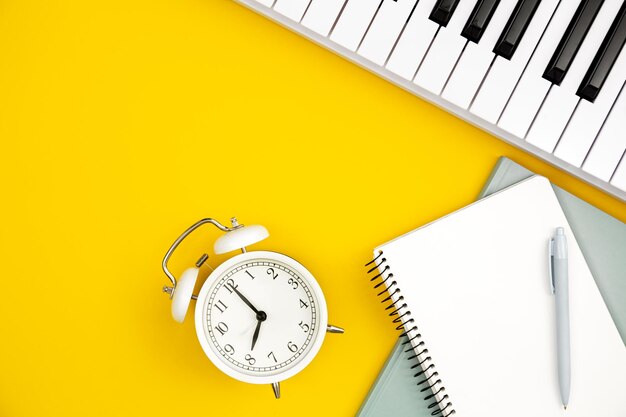 White alarm clock notebooks and piano on a yellow background concept of music education