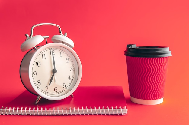 White alarm clock paper cup and notepad on a blurred background