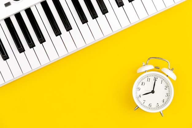 White alarm clock and piano on a yellow background top view the concept of music education and creativity white synthesizer flat lay