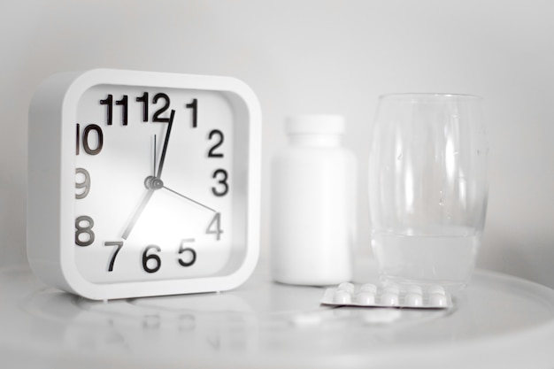 White alarm clock and pills with glass of water on table. It's time to take the medicine.