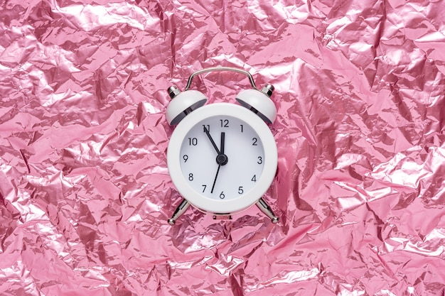 White alarm clock on pink crumpled foil background.