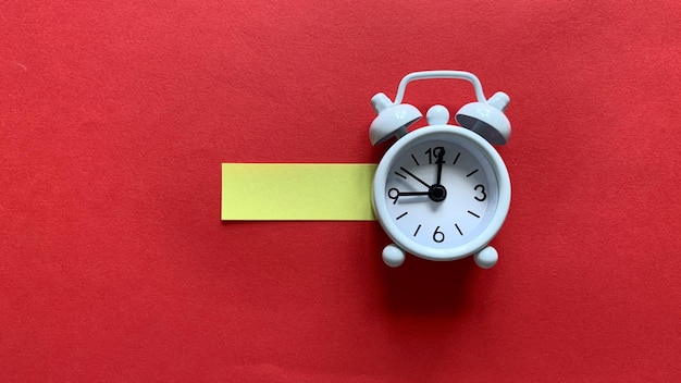 Foto orologio sveglia bianco su sfondo rosso con piccolo concetto di spazio di copia di carta gialla
