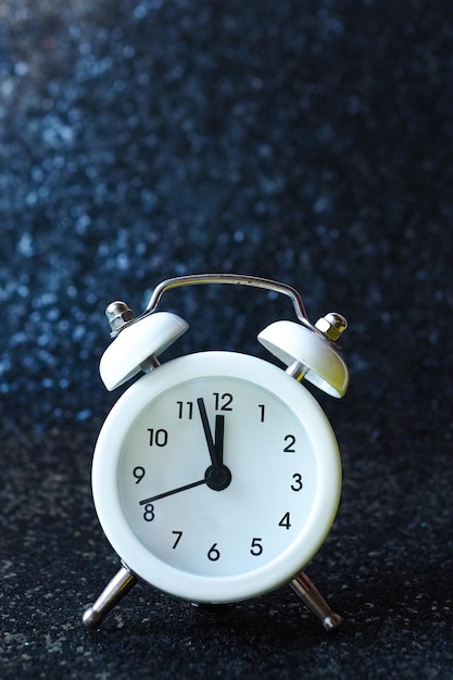 White alarm clock rings on a black shiny background. wake up concept.