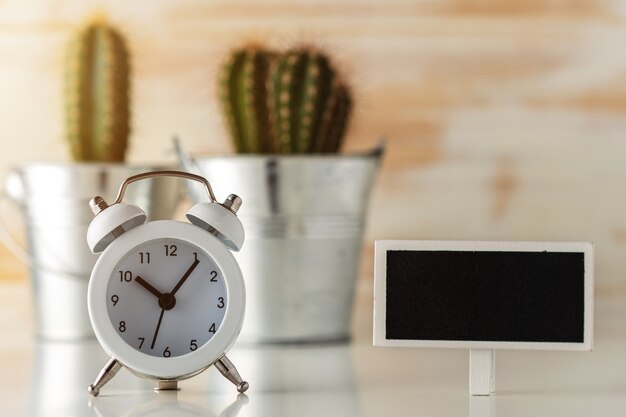 Photo white alarm clock with cactus in pot on wooden desk.