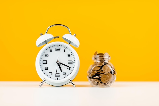 White alarm clock and yellow background money coin saving concept