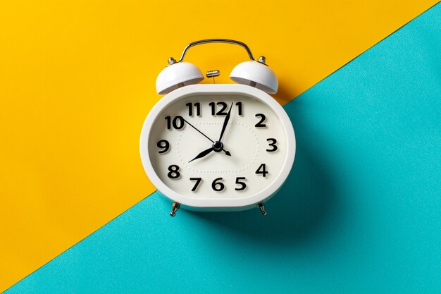 White alarm clock on yellow and blue background.