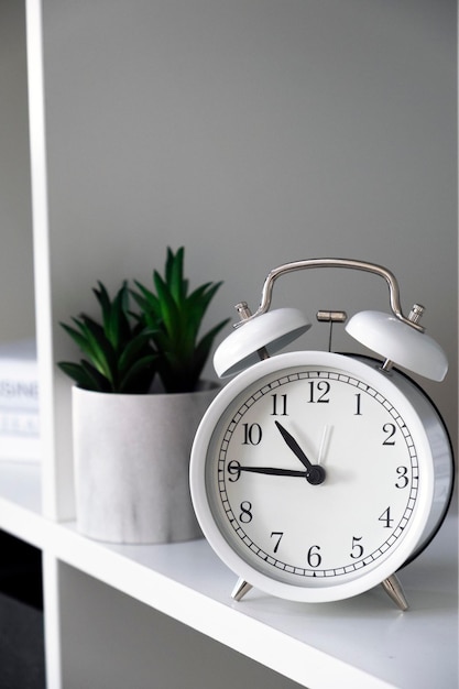 Photo white alarmclock with books and green plants on shelves