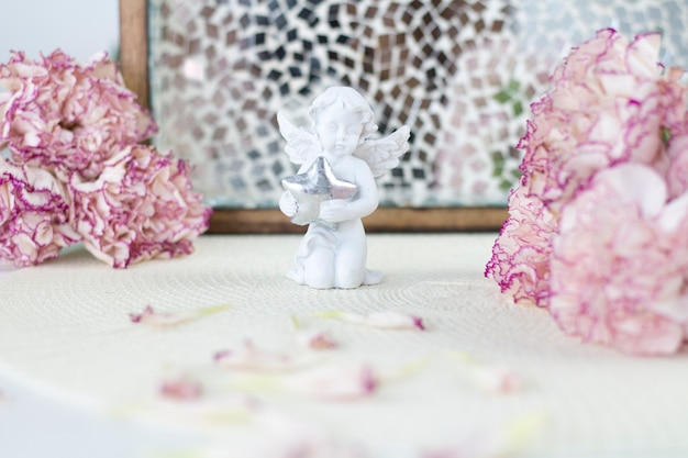 White angel on desk. Beautiful pink flowers on white desk.