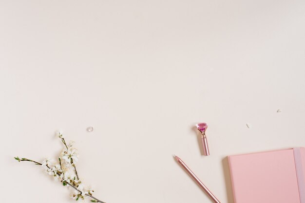 Photo white apple blossoms, a pink notepad and a pink pen on a beige background