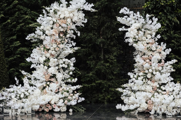 A white arch with white flowers and a green tree in the background.