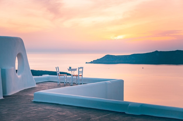 White architecture in romantic sunset light on Santorini island, Greece. Couple chairs on caldera