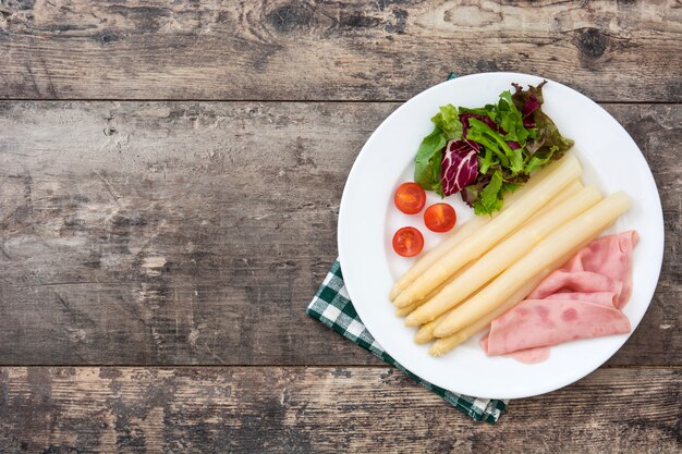 White asparagus with salad and ham on wooden table copy space