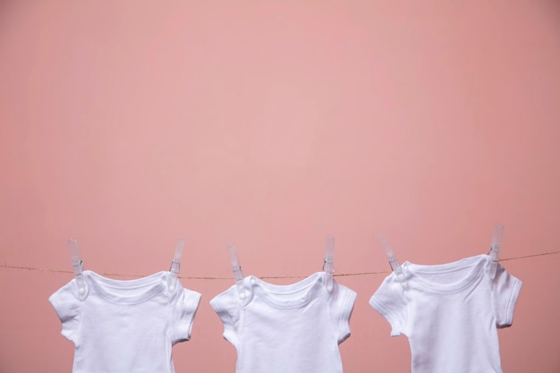 분홍색 배경에 줄에 매달려 있는 흰색 아기 바디 슈트