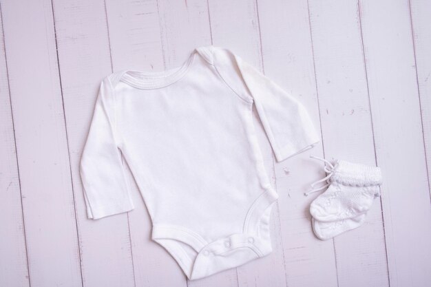 White baby bodysuit mockup for logo text or design on wooden background top view