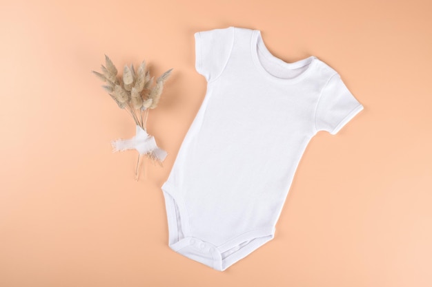Photo white baby bodysuit mockup on neutral beige pastel color background with dry plants modern boho