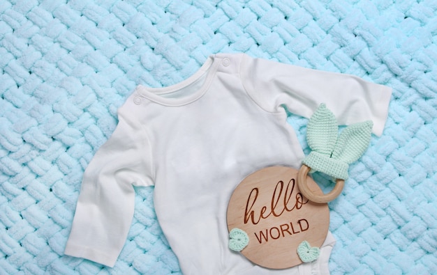 Foto white baby bodysuiteco giocattoli di legno tavoletta di legno hello world su sfondo blu morbido plaid