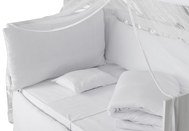 Белая детская кроватка с подушкой, пуховым одеялом и мушкетером, изолированными на белом фоне. Детальный вид.