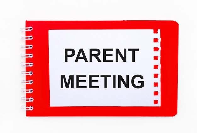 On a white background - a bright red notebook on a spiral. On it is a white sheet of paper with the text PARENT MEETING