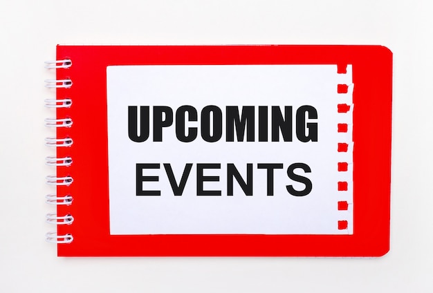 Photo on a white background - a bright red notebook on a spiral. on it is a white sheet of paper with the text upcoming events