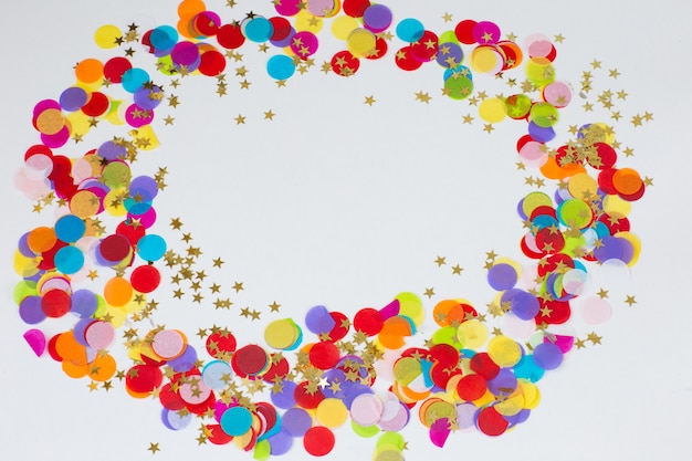 On a white background colored confetti and golden stars are lined up in a circle