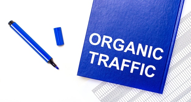 흰색 배경 보고서에는 ORGANIC TRAFFIC이라는 텍스트가 있는 파란색 펜과 파란색 노트북이 있습니다. 비즈니스 개념입니다. 배너