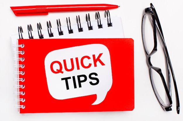 Photo on a white background, white and red notepads, black glasses, a red pen and a white card with the text quick tips