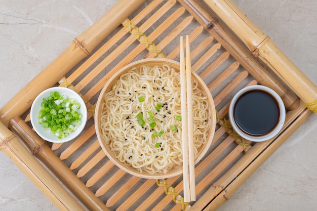 White bamboo plate bowl with egg noodles and plates with ingredients for it on a bamboo serving tray against a light background