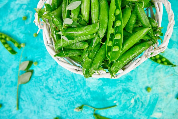 Photo white basket with fresh green peas on blue background.