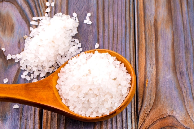 White bath salt in a wooden spoon on wooden table