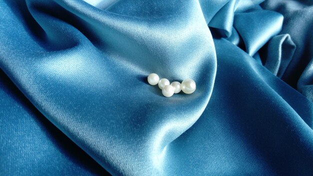 White beads lie on a blue silk fabric Jewelry on the curtains A beautiful combination of pearlescent shimmer and light tint on a silky surface Creases and waves on the fabric