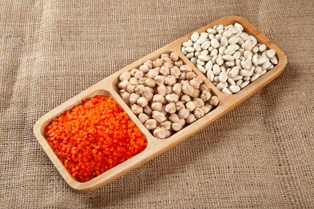 White beans dried chickpeas and red lentils on a wooden plate