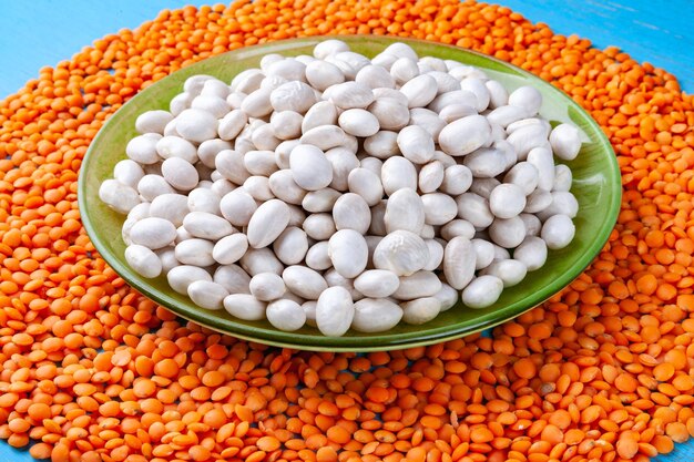 White beans in a green plate and red lentils on a blue wooden\
background