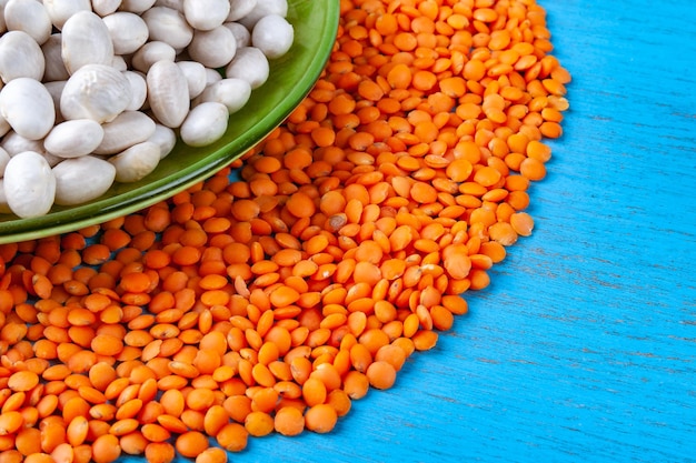 White beans in a green plate and red lentils on a blue wooden background