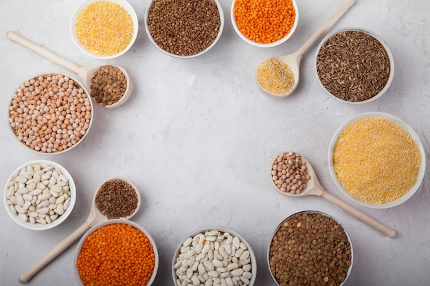 Photo white beans, peas, lentils, buckwheat, corn grits cups and wooden spoons on a white background