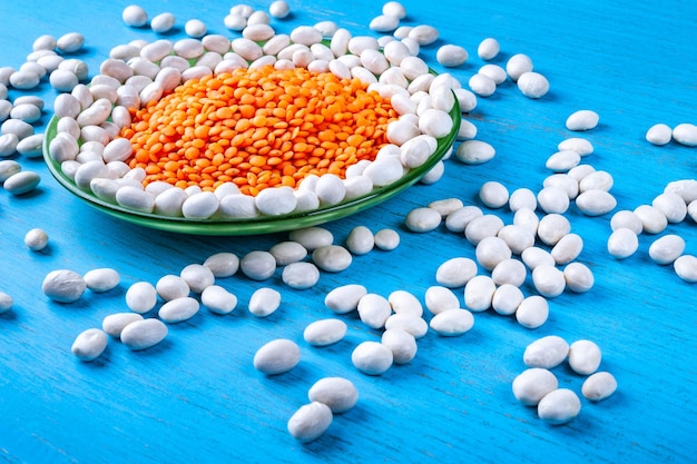 White beans and red lentils in a green plate on a blue wooden background