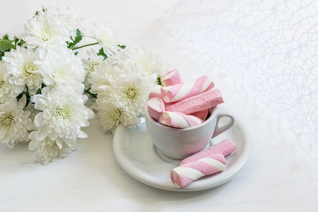 Foto bouquet di crisantemi bianchi belli e marshmallow in tazza su fondo bianco. bel biglietto di auguri per san valentino o festa della mamma.