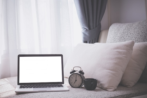 White bed with blank screen on laptop and alarm clock in bedroom.