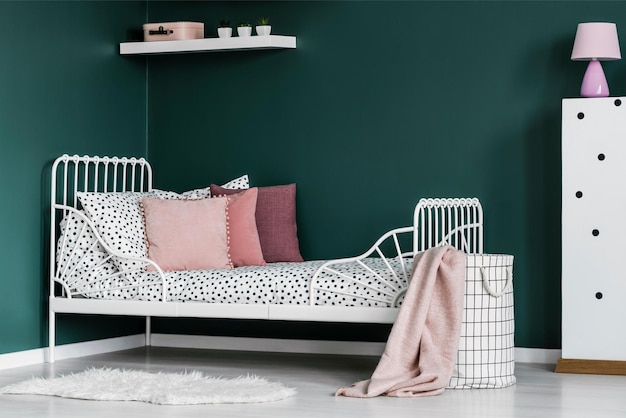 A white bed with a white frame and a white shelf with a pink pillow on it.