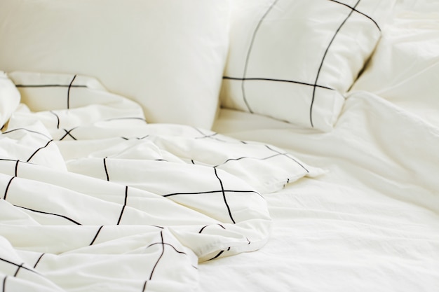 White bedding sheets with striped blanket and pillow. Messy bed.