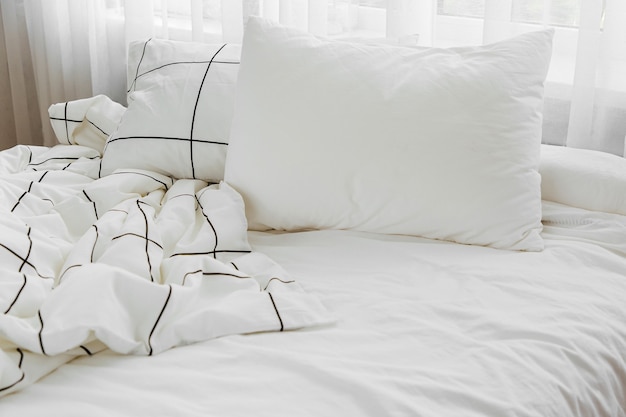 Photo white bedding sheets with striped blanket and pillow. messy bed.