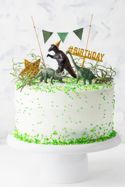 Torta di compleanno bianca con decorazioni verdi, stella d'oro e dinosauri  su un supporto per torta